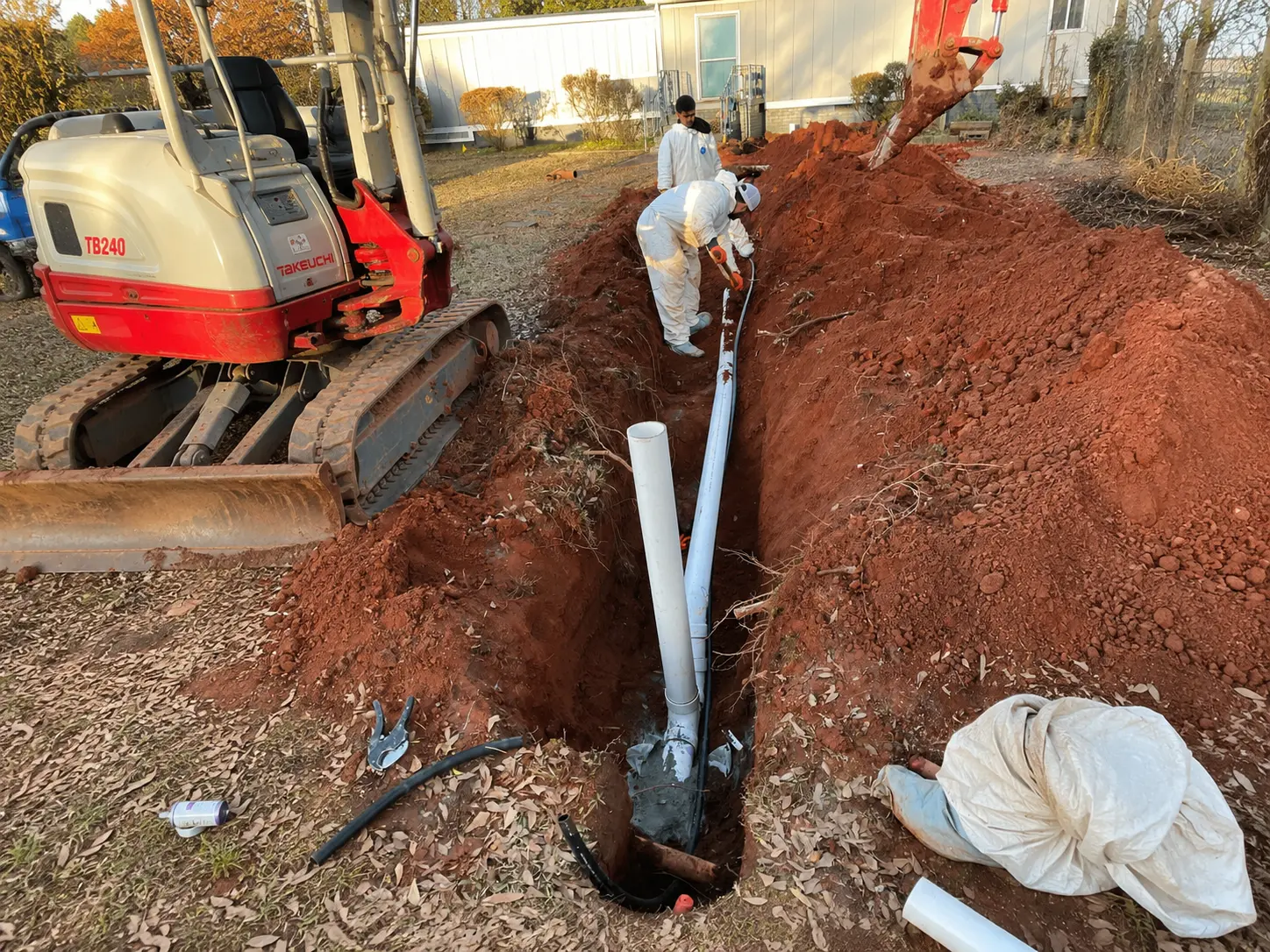Crew installing sewer pipe in red clay trench