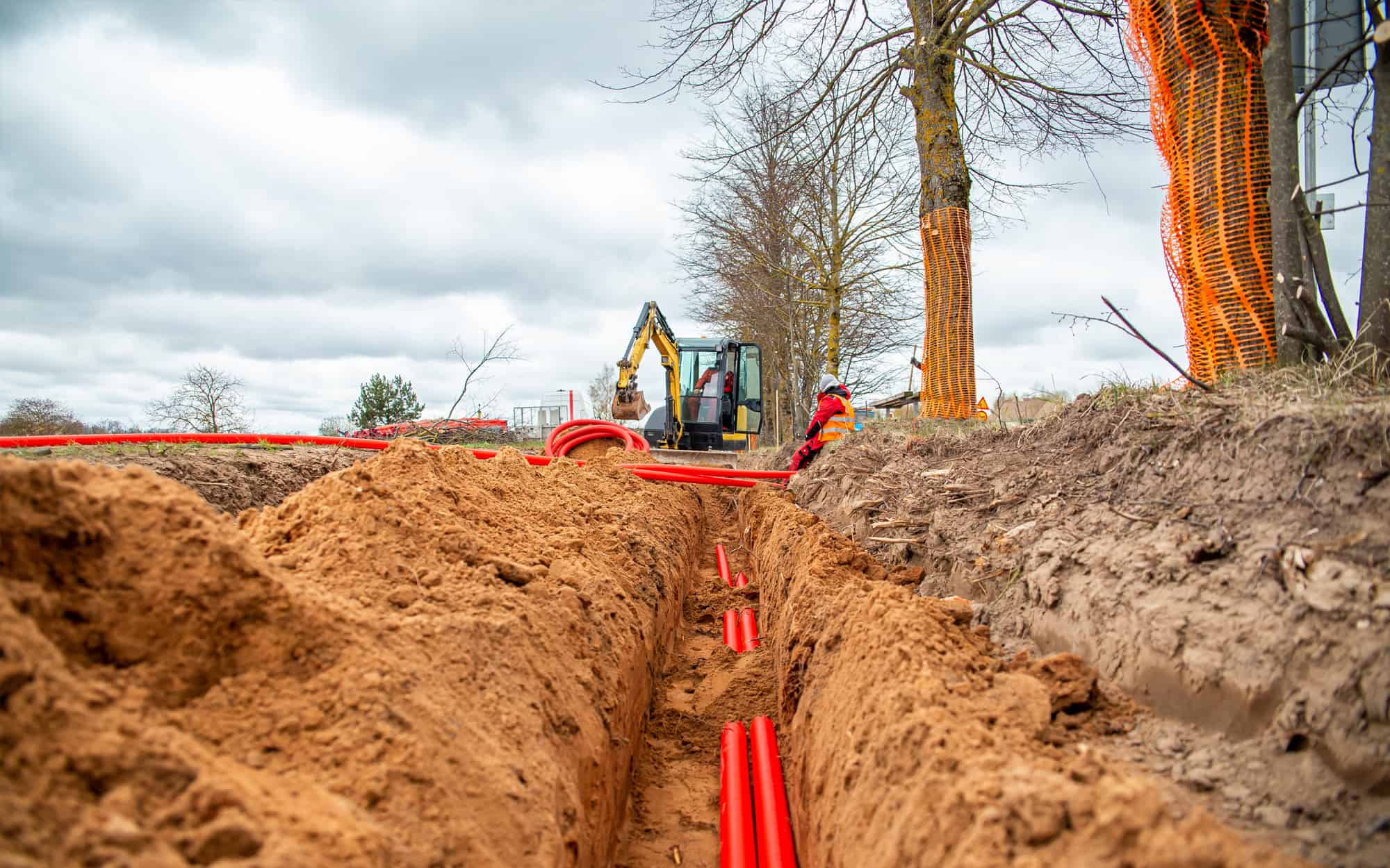 Red conduit laid in open trench with excavator